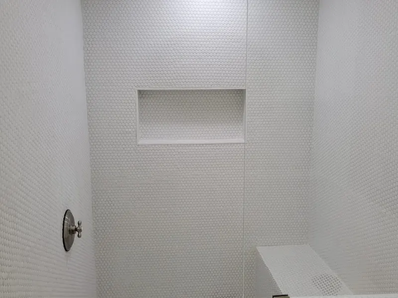 All-white penny tile shower with rain shower head and built-in niche — bathroom repair by South Blue Enterprises in Deerfield Beach, FL