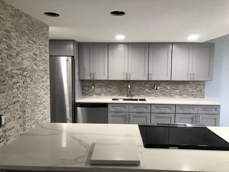 Quartz waterfall countertop with stone backsplash and gray cabinetry — stone countertop installation by South Blue Enterprises in Broward County, FL