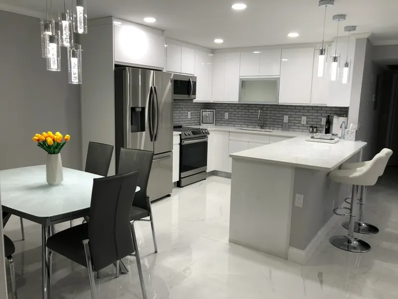 Modern white kitchen with marble countertops, pendant lighting and dining area — kitchen cabinet installation by South Blue Enterprises in Deerfield Beach, FL
